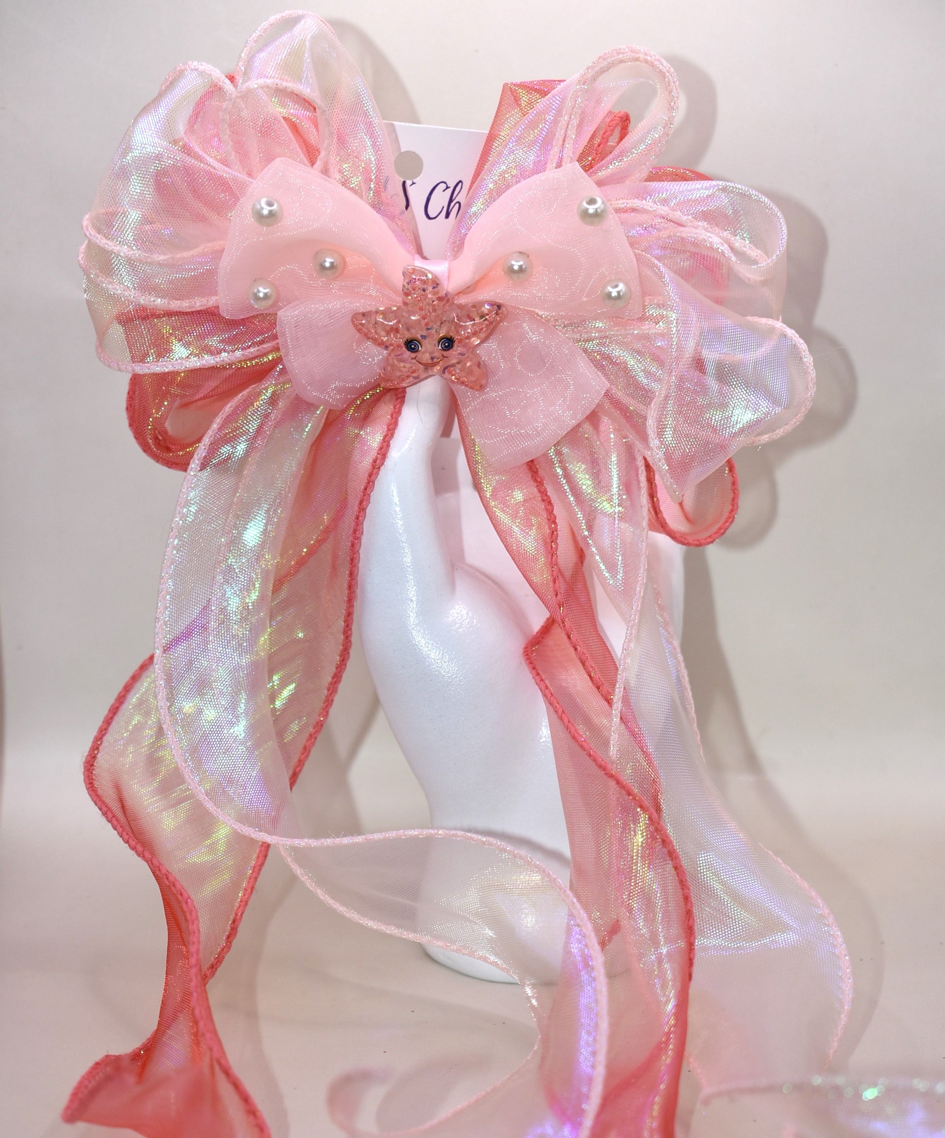 Dive into charm with this ocean-inspired long tail bow! 🌊 Layers of iridescent and sheer ribbons create a magical shimmer, topped with a delicate pearl chiffon bow 🎀. A sparkly starfish charm ✨ adds the perfect touch of seaside sparkle. Easy to wear with a wrapped alligator clip on the back. Fall head over fins for this beauty! 🐚💙