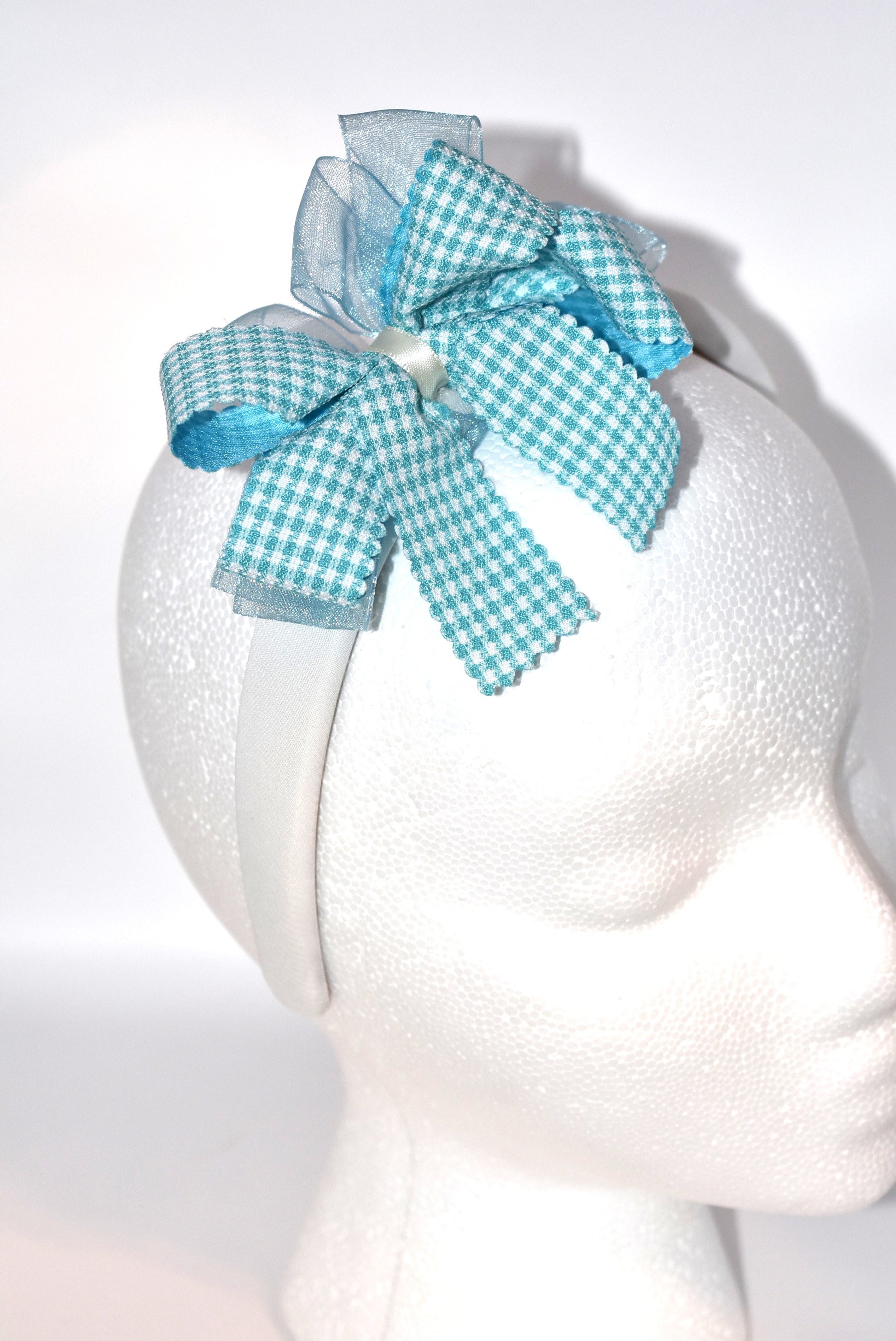 Add a splash of charm with this soft off-white headband topped with a cheerful aqua checkered ribbon. Lightweight and comfy, it’s perfect for all-day wear while adding a playful touch to any outfit.