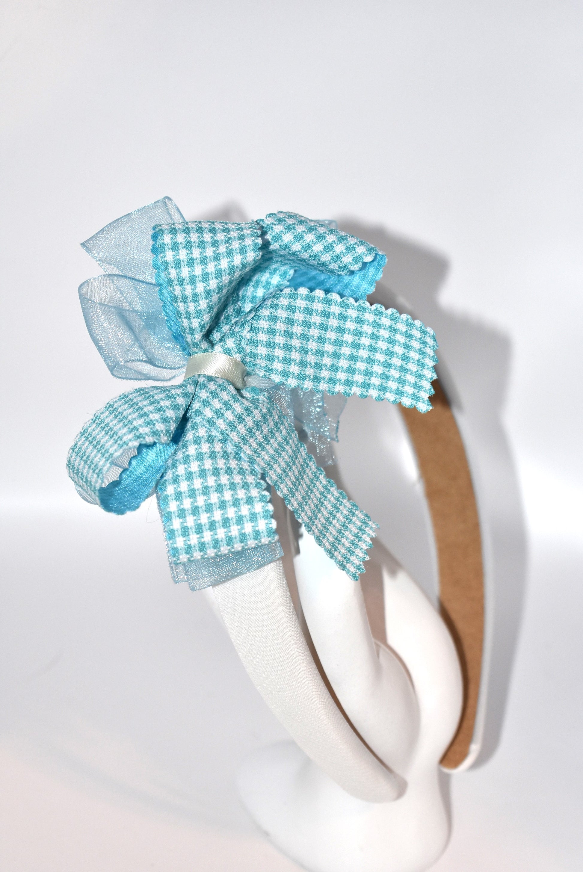 Add a splash of charm with this soft off-white headband topped with a cheerful aqua checkered ribbon. Lightweight and comfy, it’s perfect for all-day wear while adding a playful touch to any outfit.