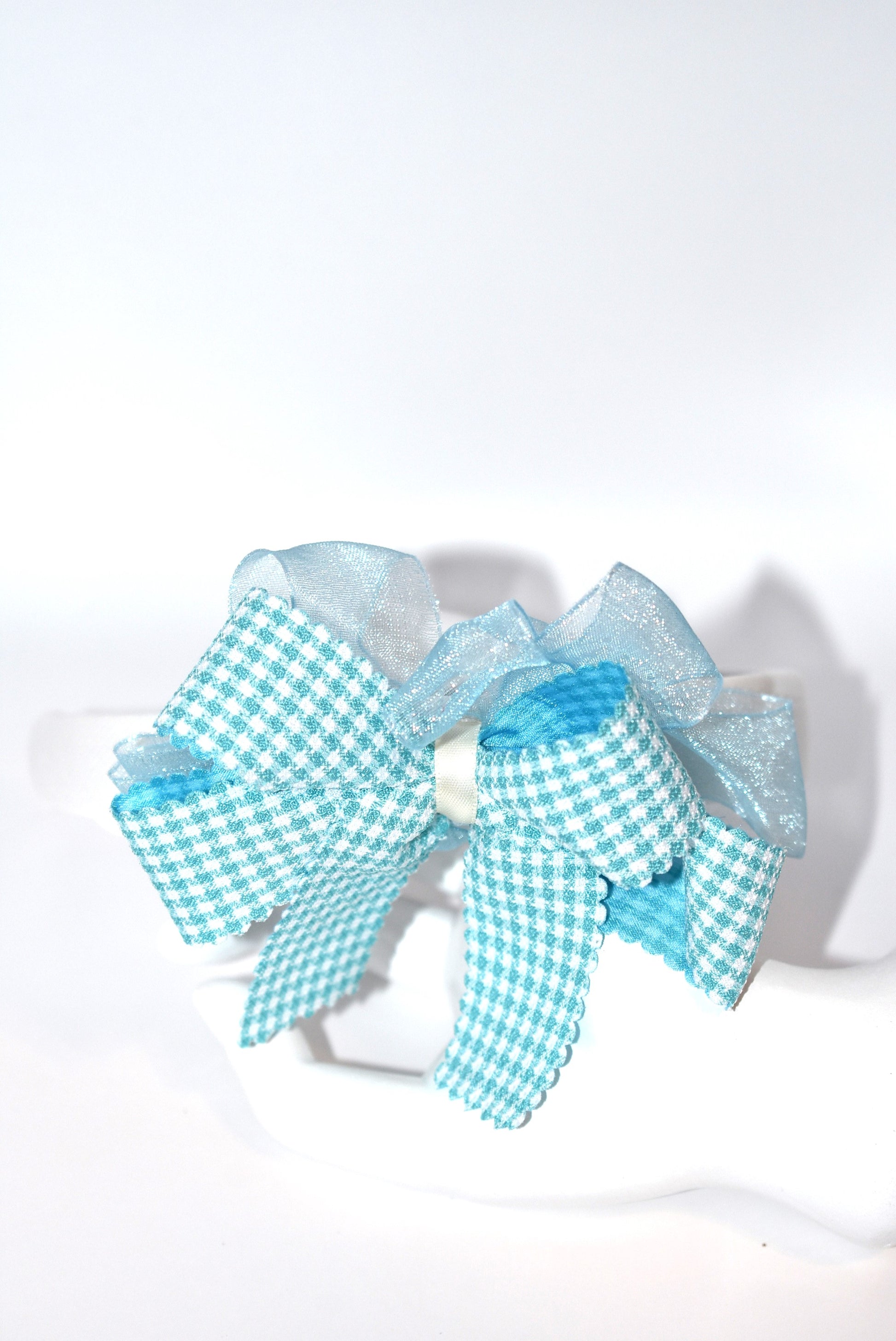Add a splash of charm with this soft off-white headband topped with a cheerful aqua checkered ribbon. Lightweight and comfy, it’s perfect for all-day wear while adding a playful touch to any outfit.