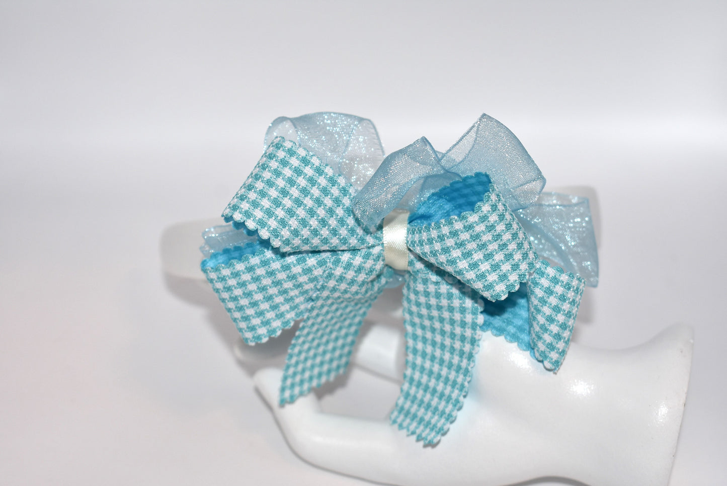 Add a splash of charm with this soft off-white headband topped with a cheerful aqua checkered ribbon. Lightweight and comfy, it’s perfect for all-day wear while adding a playful touch to any outfit.