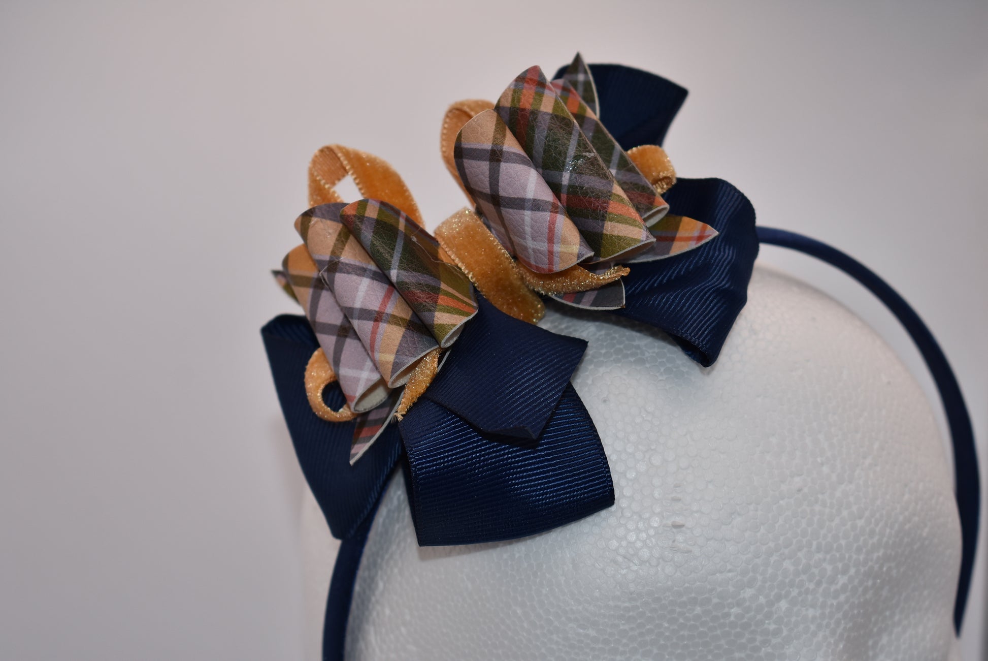Add a splash of autumn charm with this navy blue satin headband from Nana's Headband Collection. Featuring a playful faux leather bow in gold and blue patterns layered with fun ribbons, it brings comfort and style perfectly suited for your little one’s fall adven