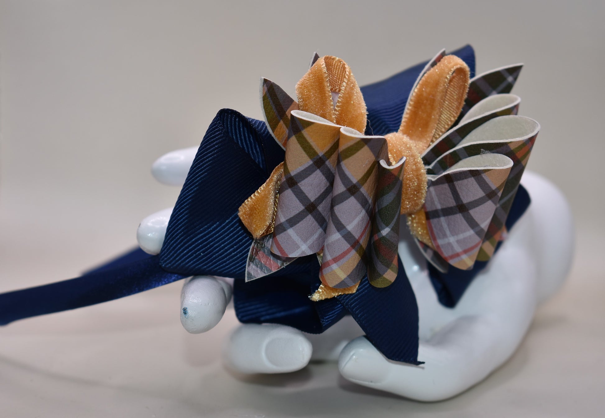 Add a splash of autumn charm with this navy blue satin headband from Nana's Headband Collection. Featuring a playful faux leather bow in gold and blue patterns layered with fun ribbons, it brings comfort and style perfectly suited for your little one’s fall adven