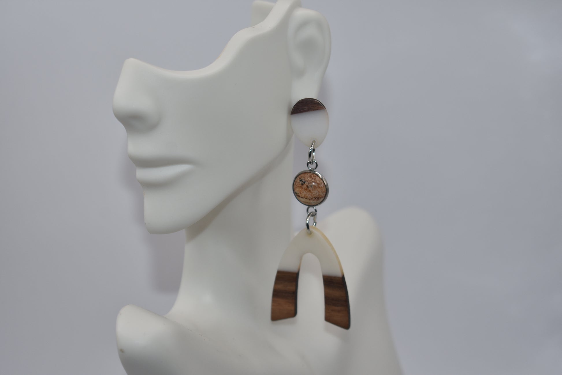 Introducing our Brown Collection earrings! Hypoallergenic, these one-of-a-kind earrings feature a natural and cream color scheme with a stunning cabochon stone in the center. Adorned with a u-shaped wood and resin charm, these earrings hang about 3 inches off the ear. A perfect finishing touch for any outfit!