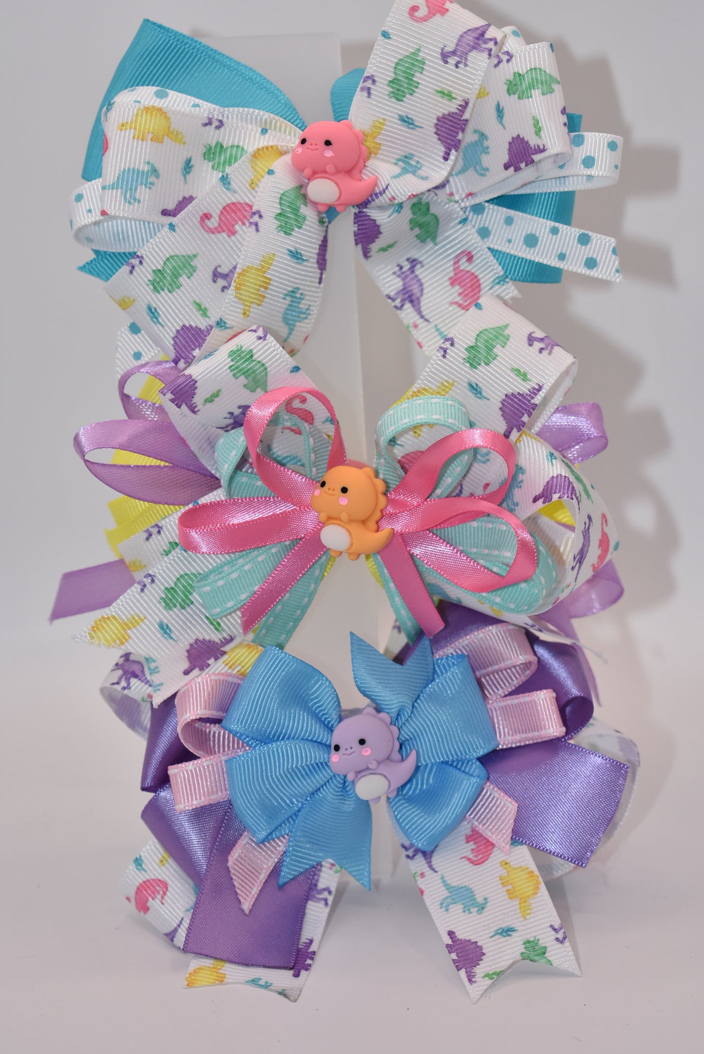 Add some prehistoric flair to any hairstyle with Nana's Collection 27! This adorable bow features multicolor layers of quality ribbon in the shape of a dinosaur, making it a playful and unique accessory. Plus, the alligator wrapped clip ensures comfortable wear all day long. Rawr!
