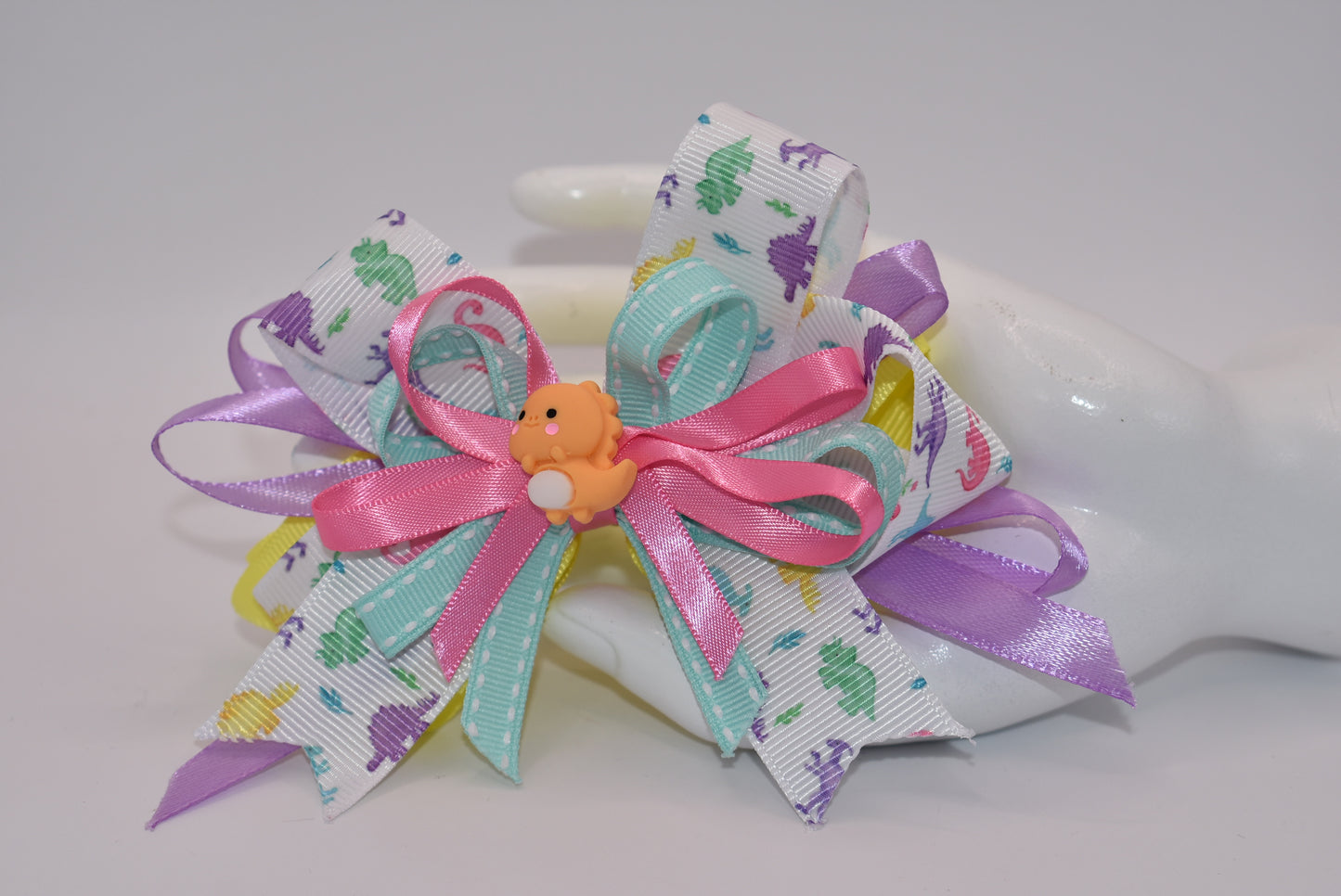 Add some prehistoric flair to any hairstyle with Nana's Collection 27! This adorable bow features multicolor layers of quality ribbon in the shape of a dinosaur, making it a playful and unique accessory. Plus, the alligator wrapped clip ensures comfortable wear all day long. Rawr!