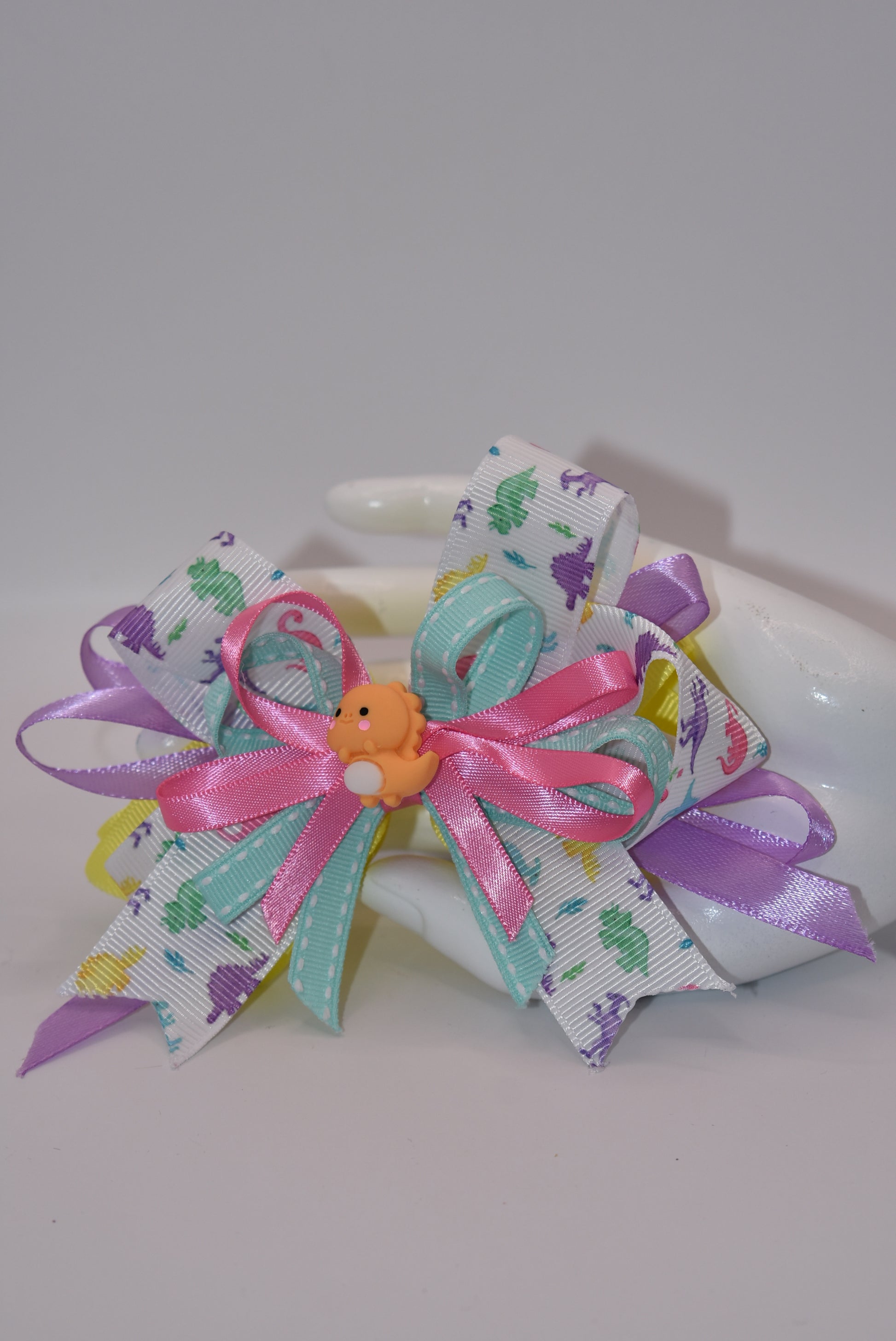 Add some prehistoric flair to any hairstyle with Nana's Collection 27! This adorable bow features multicolor layers of quality ribbon in the shape of a dinosaur, making it a playful and unique accessory. Plus, the alligator wrapped clip ensures comfortable wear all day long. Rawr!
