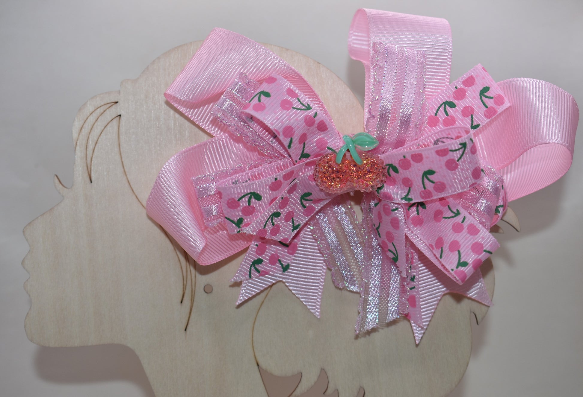 Adorable cherry-themed bow featuring delicate layers of soft pink ribbon that create a charming, dimensional look. The covered alligator clip ensures comfortable wear throughout the day without slipping or pinching. Perfect for adding a sweet pop of personality to any hairstyle, this precious accessory is designed to make you smile every time you catch your reflection. A delightful addition to Nana's Collection that celebrates timeless charm and playful style.