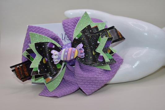 Get ready for spooky sweetness with this playful Halloween bow! 🎃 Layers of candy-inspired faux leather pop against a vibrant purple backdrop, adding a fun twist to your festive look. 🍬 Easily clip it on with a handy alligator clip for quick and comfy wear. Perfect for trick-or-treating or party fun! 🍭
