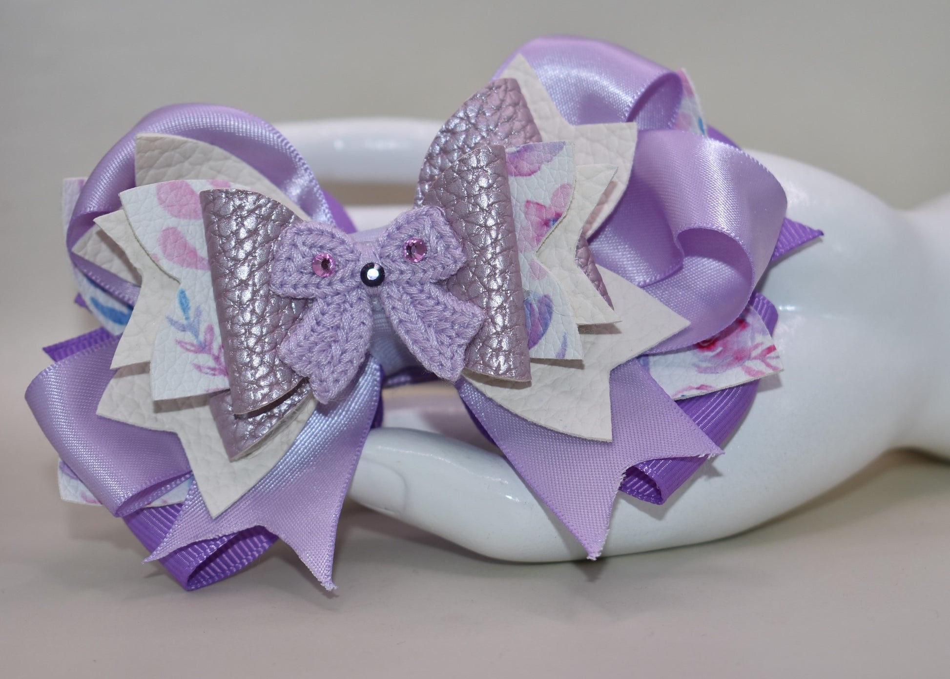 Bow lovers, rejoice! 🎀 This stunning creation features luxurious layers of ribbon and faux leather that build the perfect foundation. Topped with an adorable crocheted lavender bow adorned with sparkles ✨ for that extra touch of magic, this accessory is pure charm. The wrapped alligator clip ensures a secure, all-day hold so you can strut your stuff without worry. Perfect for adding a playful pop of personality to any look! 💜