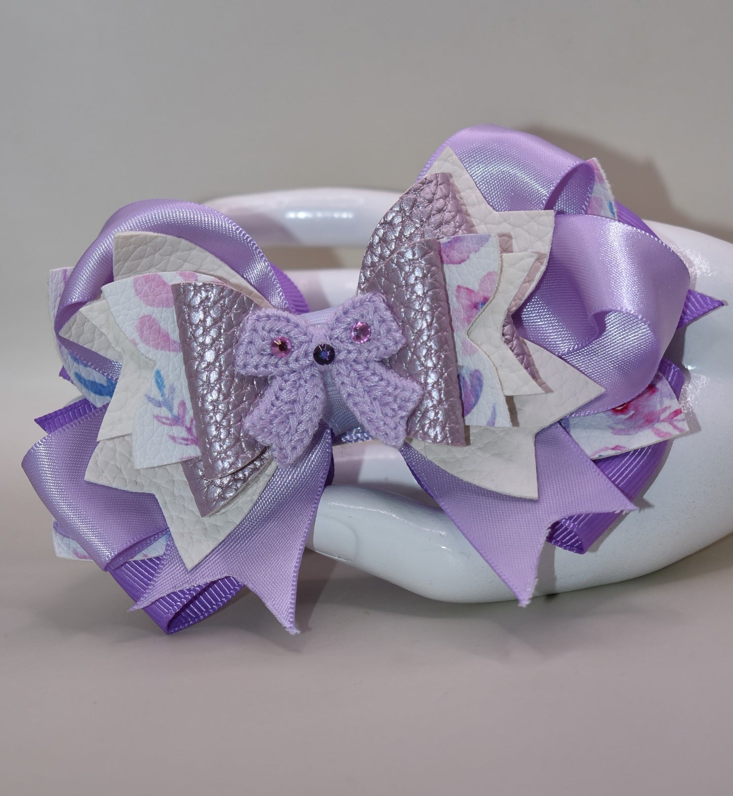Bow lovers, rejoice! 🎀 This stunning creation features luxurious layers of ribbon and faux leather that build the perfect foundation. Topped with an adorable crocheted lavender bow adorned with sparkles ✨ for that extra touch of magic, this accessory is pure charm. The wrapped alligator clip ensures a secure, all-day hold so you can strut your stuff without worry. Perfect for adding a playful pop of personality to any look! 💜
