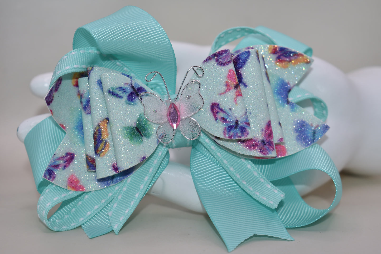 Introducing the Nana's Collection 40 – a super pretty aqua butterfly bow that's ready to flutter into your heart! 🦋✨ This charming accessory features layered butterfly-themed faux leather with a matching aqua ribbon that ties everything together beautifully. The showstopper? An absolutely gorgeous butterfly perched right on top to complete the look. Whether you're dressing up for a special occasion or adding a whimsical touch to your everyday style, this bow is the perfect finishing flourish for any outfit