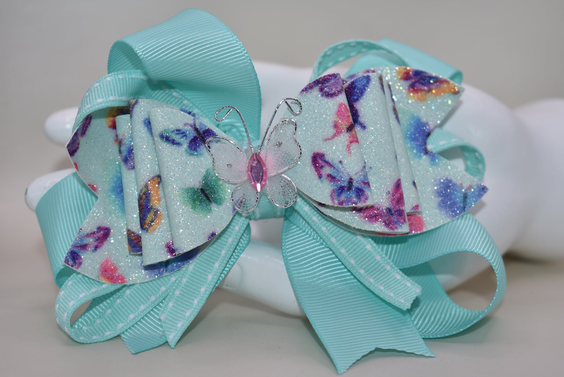 Introducing the Nana's Collection 40 – a super pretty aqua butterfly bow that's ready to flutter into your heart! 🦋✨ This charming accessory features layered butterfly-themed faux leather with a matching aqua ribbon that ties everything together beautifully. The showstopper? An absolutely gorgeous butterfly perched right on top to complete the look. Whether you're dressing up for a special occasion or adding a whimsical touch to your everyday style, this bow is the perfect finishing flourish for any outfit