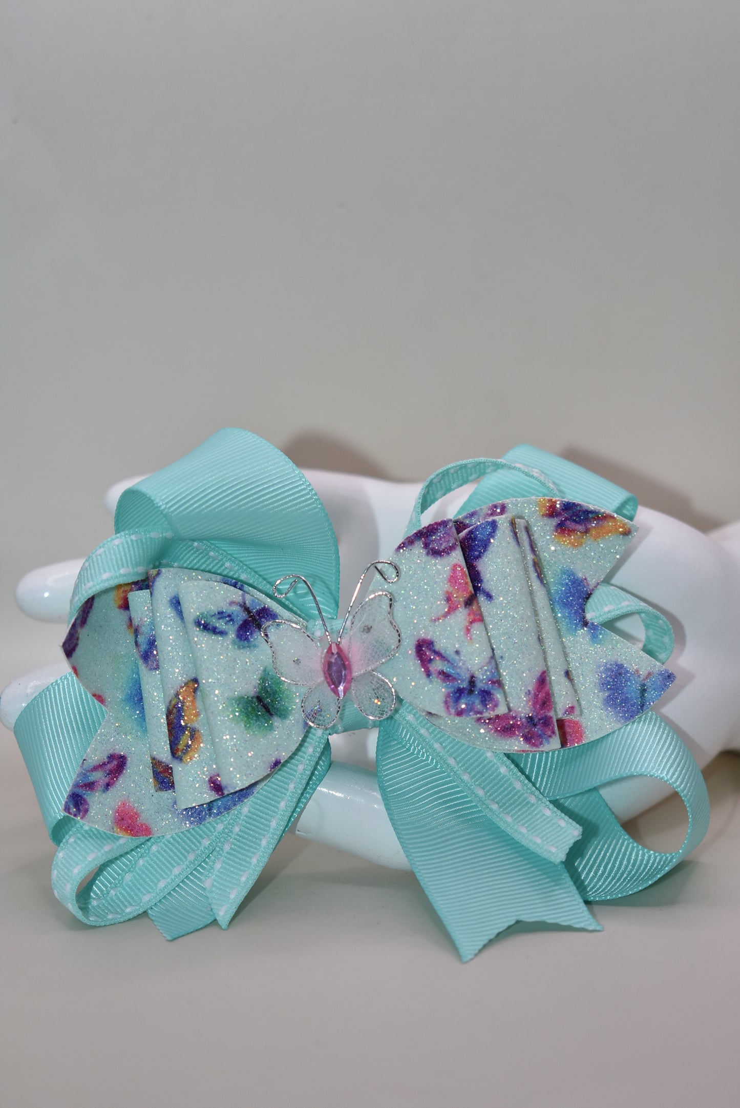 Introducing the Nana's Collection 40 – a super pretty aqua butterfly bow that's ready to flutter into your heart! 🦋✨ This charming accessory features layered butterfly-themed faux leather with a matching aqua ribbon that ties everything together beautifully. The showstopper? An absolutely gorgeous butterfly perched right on top to complete the look. Whether you're dressing up for a special occasion or adding a whimsical touch to your everyday style, this bow is the perfect finishing flourish for any outfit