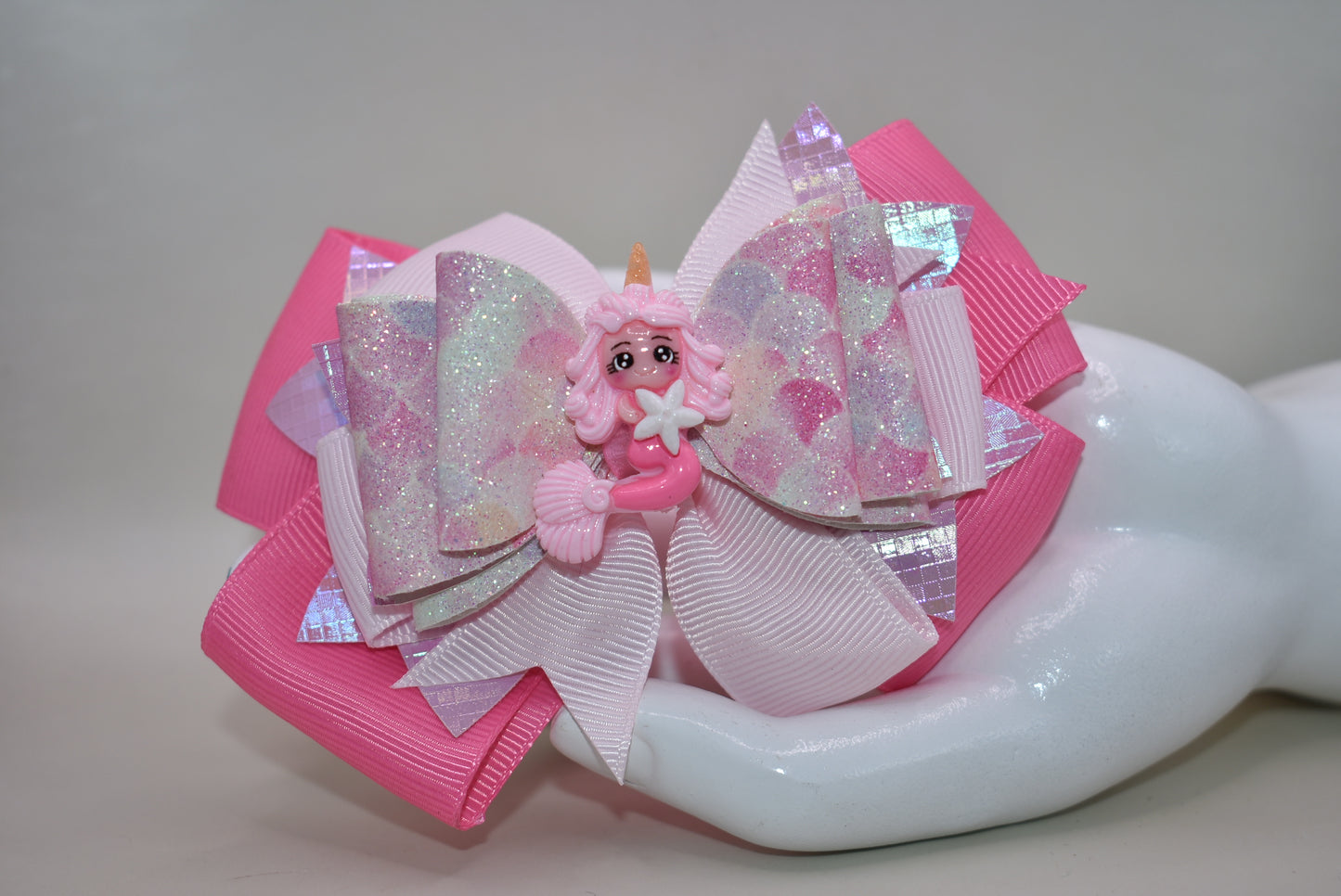 Dive into whimsy with this enchanting mermaid bow! 🧜♀️✨ Featuring layers of luxe faux leather and silky ribbon, this playful accessory is topped with an adorable pink mermaid charm that brings ocean magic to any hairstyle. The covered alligator clip ensures all-day comfort without slipping, making it perfect for little mermaids everywhere. 🎀💕 A splash of charm that's as sweet as the sea!