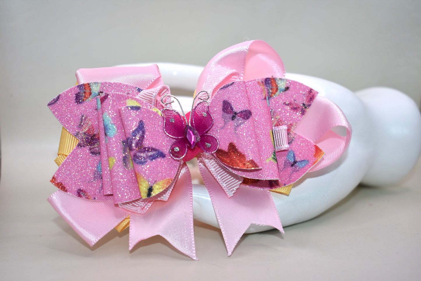 ✨ Introducing the prettiest addition to your hair collection! This adorable pink butterfly bow features layers of mixed faux leather and ribbon that create dimension and charm. A delicate butterfly charm sits proudly on top, adding that extra touch of whimsy. 🦋 The wrapped alligator clip keeps your style secure all day long, so you can twirl and play without worry. Perfect for adding a pop of personality to any look! 💕