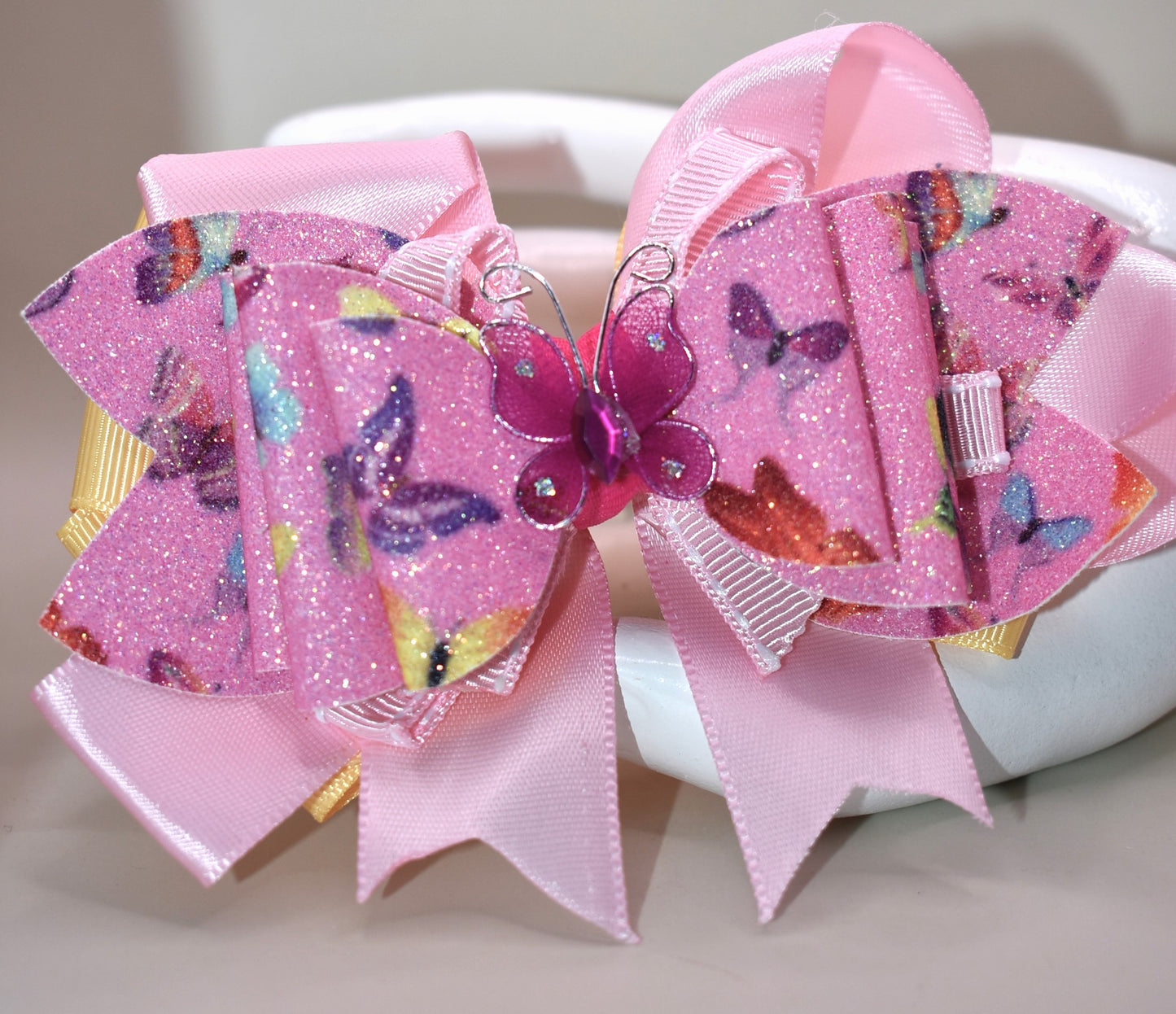 ✨ Introducing the prettiest addition to your hair collection! This adorable pink butterfly bow features layers of mixed faux leather and ribbon that create dimension and charm. A delicate butterfly charm sits proudly on top, adding that extra touch of whimsy. 🦋 The wrapped alligator clip keeps your style secure all day long, so you can twirl and play without worry. Perfect for adding a pop of personality to any look! 💕