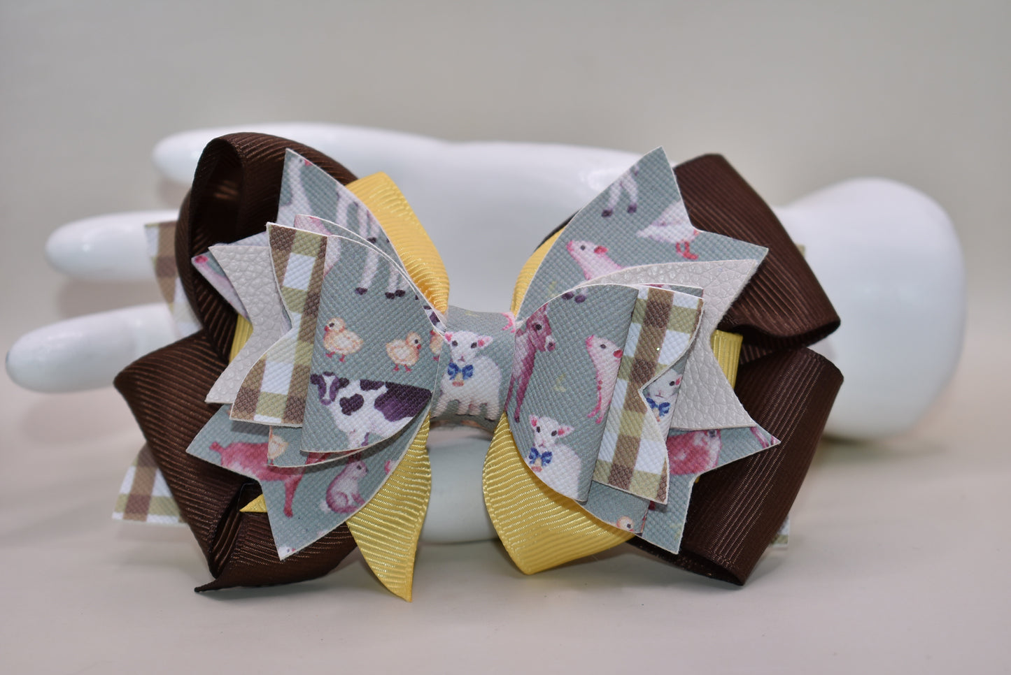 Meet the bow that'll have every farmer grinning from ear to ear! 🌾 This adorable one-of-a-kind animal-themed bow is bursting with personality, featuring layers upon layers of luxe ribbon and faux leather that create serious style depth. 🎀 Whether you're heading to the barn, a country event, or just want to add a touch of whimsy to your everyday look, this charming accessory transforms any outfit into something special. 🐄✨ Nana's Collection brings that perfect blend of cute and quirky that makes you smile