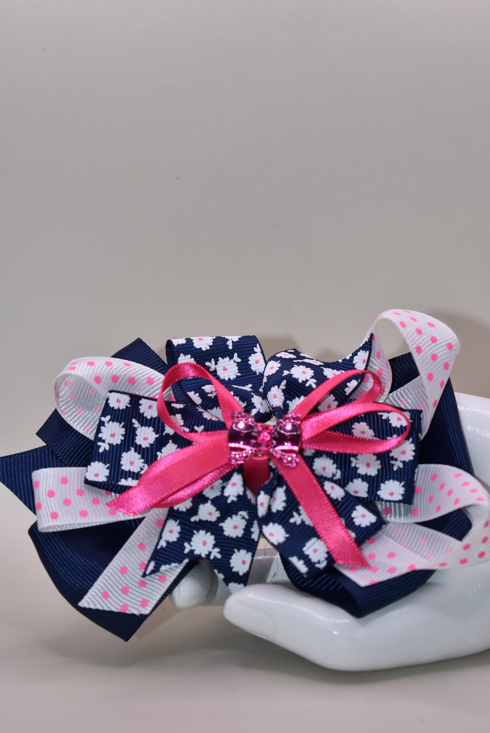 This adorable bow clip is a playful mix of navy blue and bright pink with layered textures featuring solid, floral, and polka dot patterns. 🎀 The cutest hot pink bow charm sits proudly on top, adding that extra pop of personality! ✨ Secured with a wrapped alligator clip, it stays put through all your adventures. Perfect for adding a fun, charming touch to any hairstyle! 💕