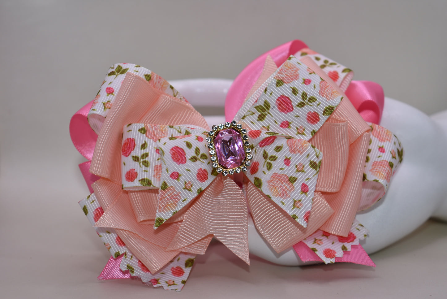 Introducing a bow that's as sweet as it is sparkly! 🌸 This charming hair clip features delicate flower motifs adorned with layers upon layers of dreamy peach and pink ribbons that dance together beautifully. A gorgeous gem sits perched on top, catching the light with every twirl and turn ✨ The wrapped alligator clip makes styling effortless—just clip and go! 💕 Perfect for adding a touch of whimsy and elegance to any hairstyle, this piece brings instant charm and personality to your look. 🎀