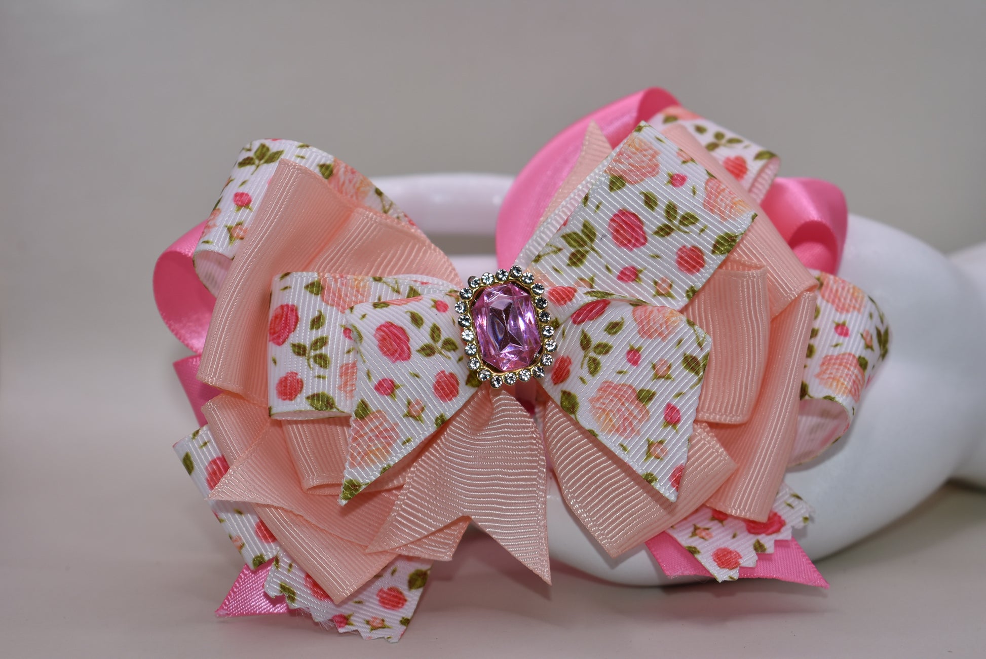Introducing a bow that's as sweet as it is sparkly! 🌸 This charming hair clip features delicate flower motifs adorned with layers upon layers of dreamy peach and pink ribbons that dance together beautifully. A gorgeous gem sits perched on top, catching the light with every twirl and turn ✨ The wrapped alligator clip makes styling effortless—just clip and go! 💕 Perfect for adding a touch of whimsy and elegance to any hairstyle, this piece brings instant charm and personality to your look. 🎀