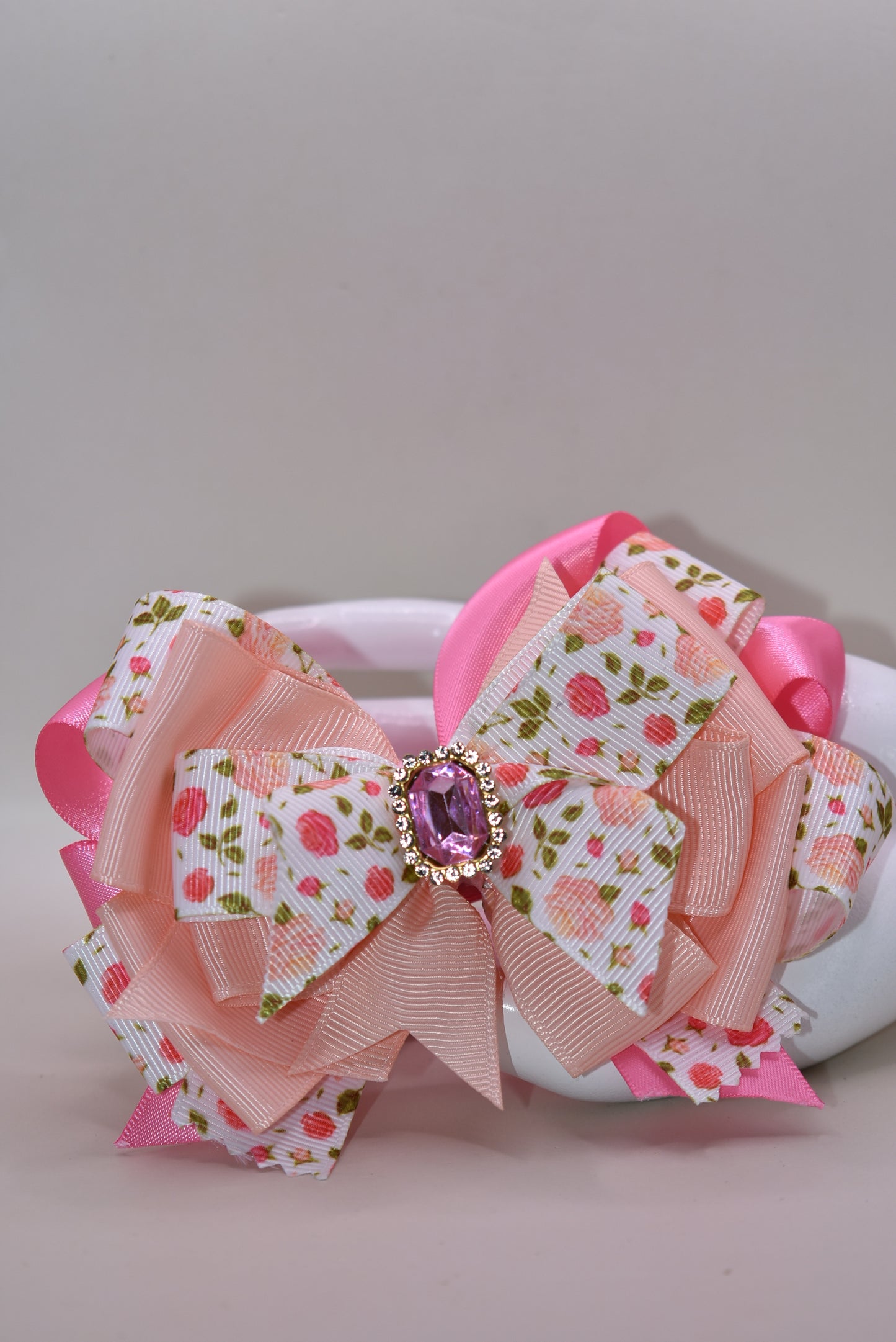 Introducing a bow that's as sweet as it is sparkly! 🌸 This charming hair clip features delicate flower motifs adorned with layers upon layers of dreamy peach and pink ribbons that dance together beautifully. A gorgeous gem sits perched on top, catching the light with every twirl and turn ✨ The wrapped alligator clip makes styling effortless—just clip and go! 💕 Perfect for adding a touch of whimsy and elegance to any hairstyle, this piece brings instant charm and personality to your look. 🎀