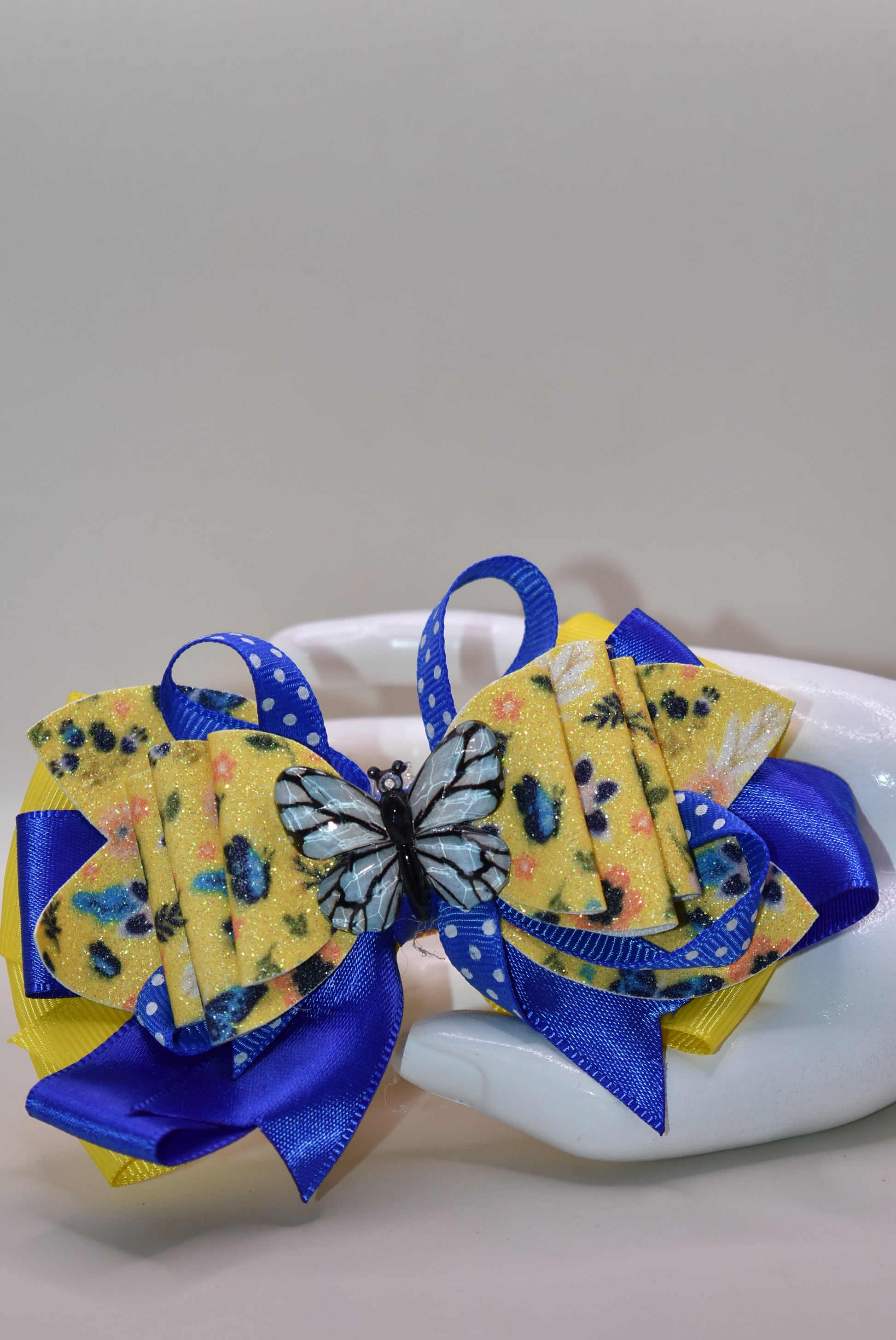 This one-of-a-kind bow brings spring vibes with vibrant layers of bright blue and yellow ribbon mixed with faux leather for texture and dimension. 🦋 A gorgeous blue butterfly charm perches perfectly on top, adding whimsical charm to any hairstyle. The alligator clip is wrapped in soft ribbon for all-day comfort, so you can wear it from morning to night without any pinching. Perfect for adding a pop of color and personality to your look! 🌈✨
