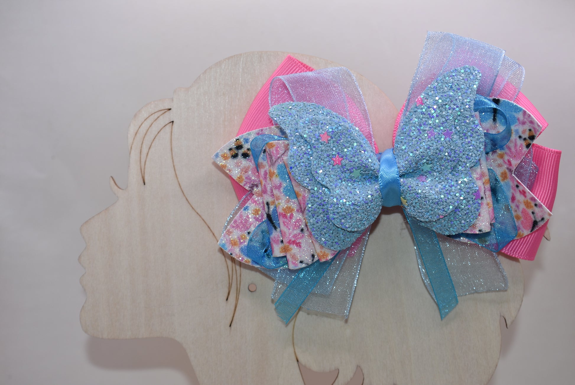✨ Introducing a one-of-a-kind bow that's pure magic! 🦋 This stunning creation features luxurious layers of ribbon and faux leather, adorned with delicate butterfly and flower motifs. The showstopper? A gorgeous glitter blue butterfly perched on top that catches the light beautifully. 💙 Secured with a wrapped alligator clip on the back, it's the perfect accessory to add whimsy and charm to any hairstyle. Each piece is uniquely crafted, making it a special treasure from Nana's Collection. 🌸