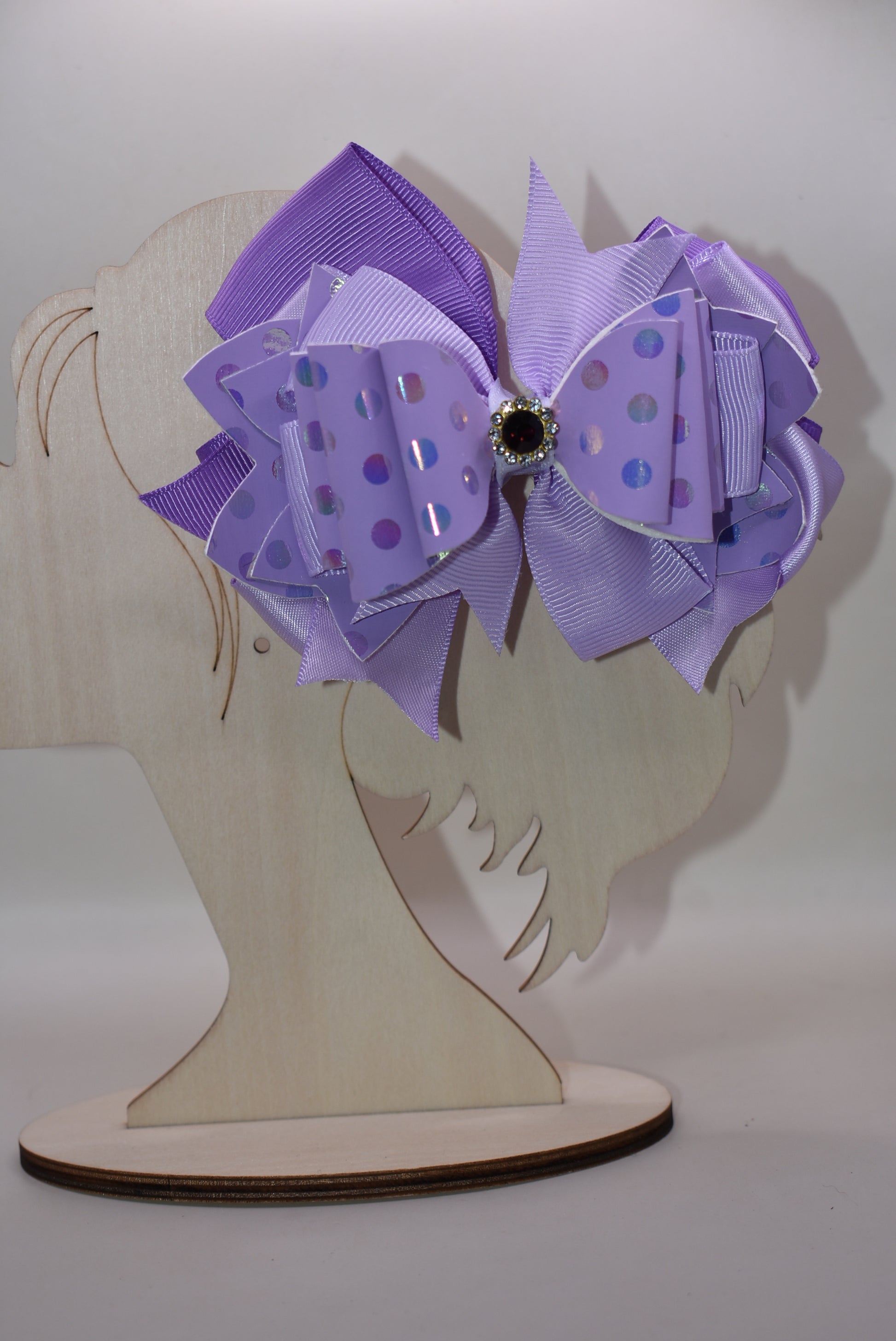 ✨ Introducing a show-stopping purple bow that's pure magic! 💜 This gorgeous accessory features a stunning lavender shade paired with luxe polka dot faux leather and cascading ribbon layers for dimensional style. A sparkling purple gem sits proudly on top, adding just the right touch of glamour and shimmer. ✨ Secured with a wrapped alligator clip for a secure, comfortable hold all day long. Perfect for adding a playful pop of color to any look! 🎀