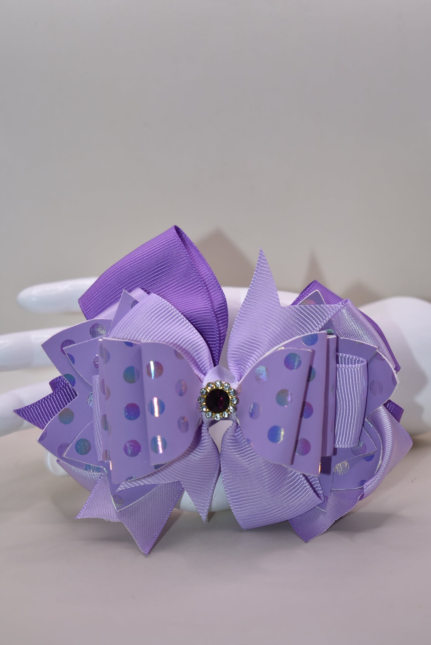 ✨ Introducing a show-stopping purple bow that's pure magic! 💜 This gorgeous accessory features a stunning lavender shade paired with luxe polka dot faux leather and cascading ribbon layers for dimensional style. A sparkling purple gem sits proudly on top, adding just the right touch of glamour and shimmer. ✨ Secured with a wrapped alligator clip for a secure, comfortable hold all day long. Perfect for adding a playful pop of color to any look! 🎀