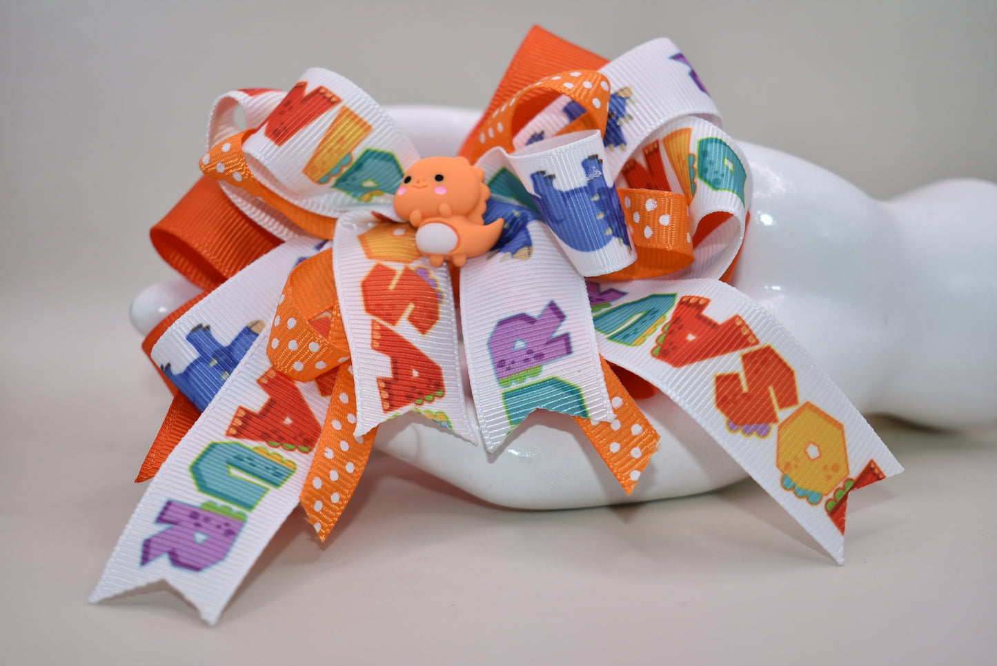 Meet your new favorite hair accessory! 🦕✨ This adorable orange dinosaur perches happily atop layers of vibrant ribbon, bringing instant joy to any hairstyle. The playful design features a wrapped alligator clip that's super easy to use—just clip and go! Perfect for adding a pop of personality and cuteness to your day. Whether you're heading to school, a playdate, or just want to smile a little brighter, this charming dino bow is ready to make your look roar with fun! 🎀😊