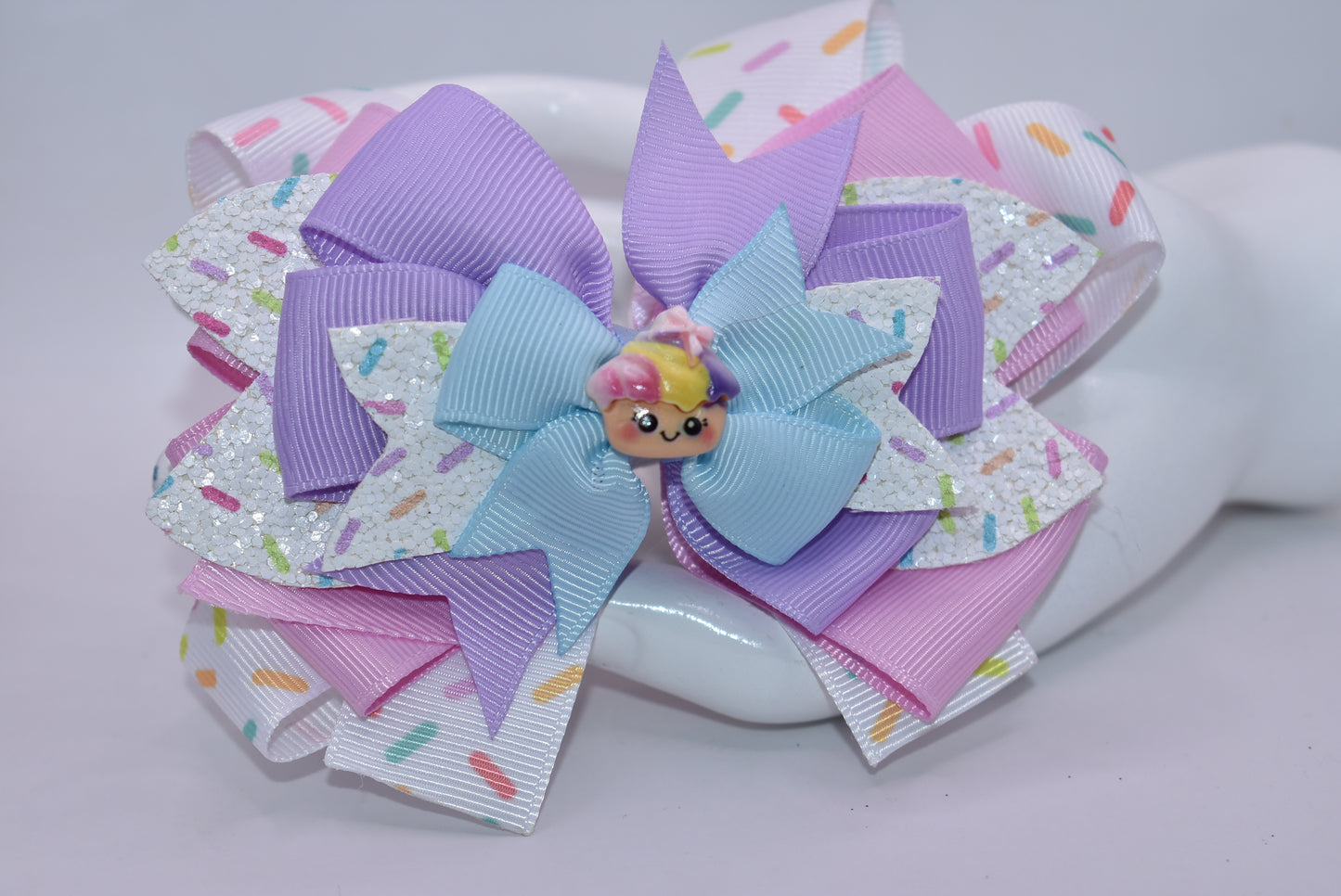 This adorably delicious sprinkle bow is pure cuteness! 🎀✨ Layered ribbon and faux leather create a textured, eye-catching design that's absolutely irresistible. A sweet little cupcake charm perches on top, adding the perfect finishing touch to this charming accessory. 🧁 The wrapped alligator clip on back ensures a secure, comfortable fit all day long. Perfect for adding a playful pop of personality to any hairstyle! 💕