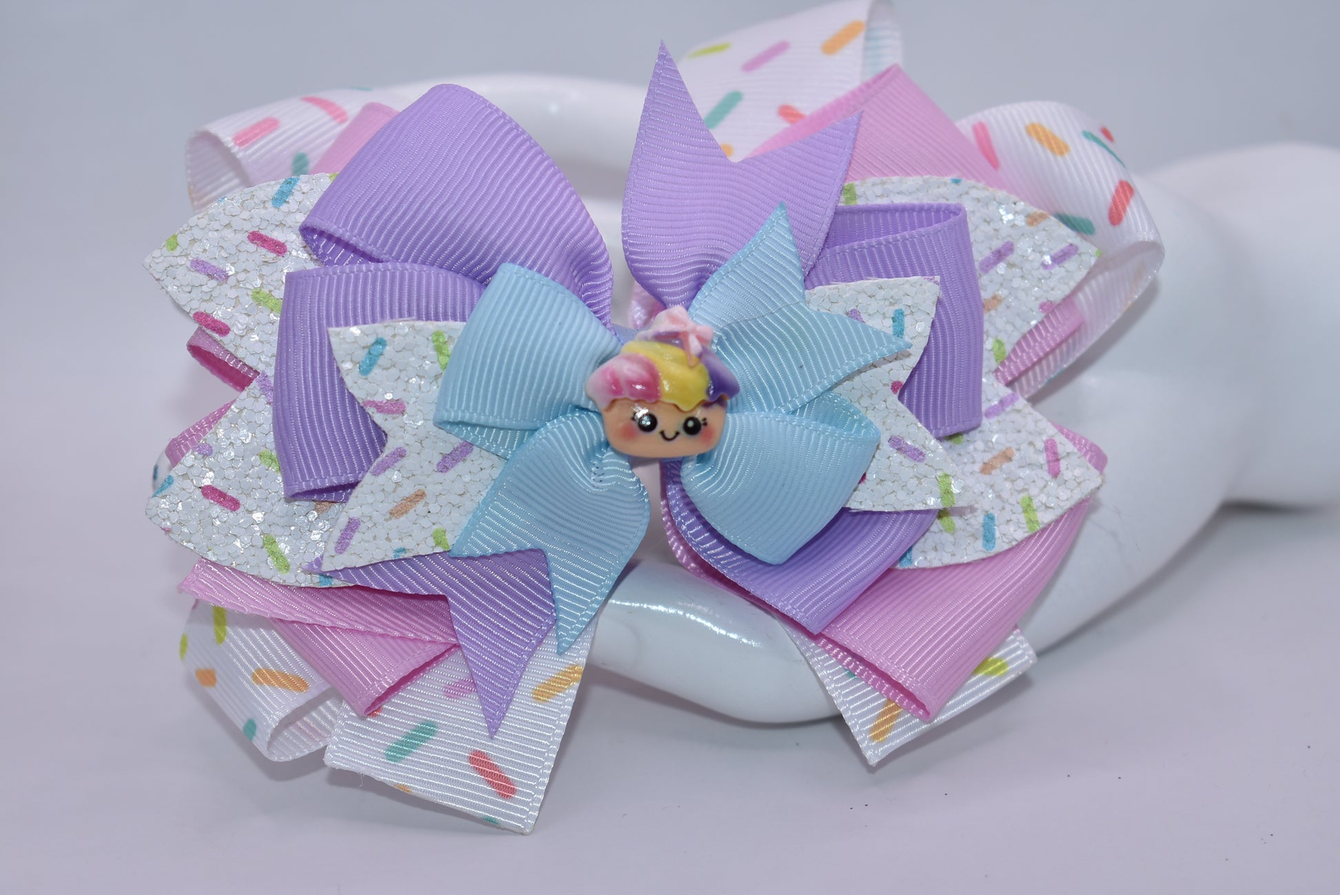 This adorably delicious sprinkle bow is pure cuteness! 🎀✨ Layered ribbon and faux leather create a textured, eye-catching design that's absolutely irresistible. A sweet little cupcake charm perches on top, adding the perfect finishing touch to this charming accessory. 🧁 The wrapped alligator clip on back ensures a secure, comfortable fit all day long. Perfect for adding a playful pop of personality to any hairstyle! 💕
