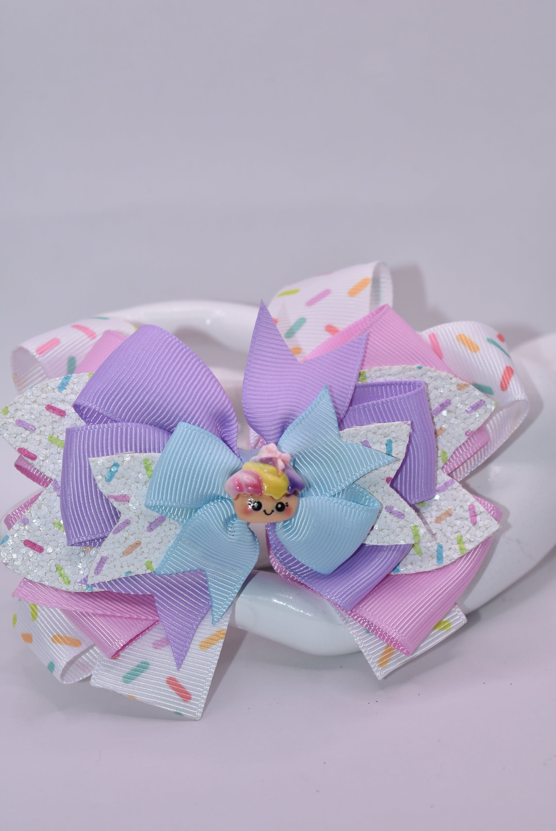 This adorably delicious sprinkle bow is pure cuteness! 🎀✨ Layered ribbon and faux leather create a textured, eye-catching design that's absolutely irresistible. A sweet little cupcake charm perches on top, adding the perfect finishing touch to this charming accessory. 🧁 The wrapped alligator clip on back ensures a secure, comfortable fit all day long. Perfect for adding a playful pop of personality to any hairstyle! 💕