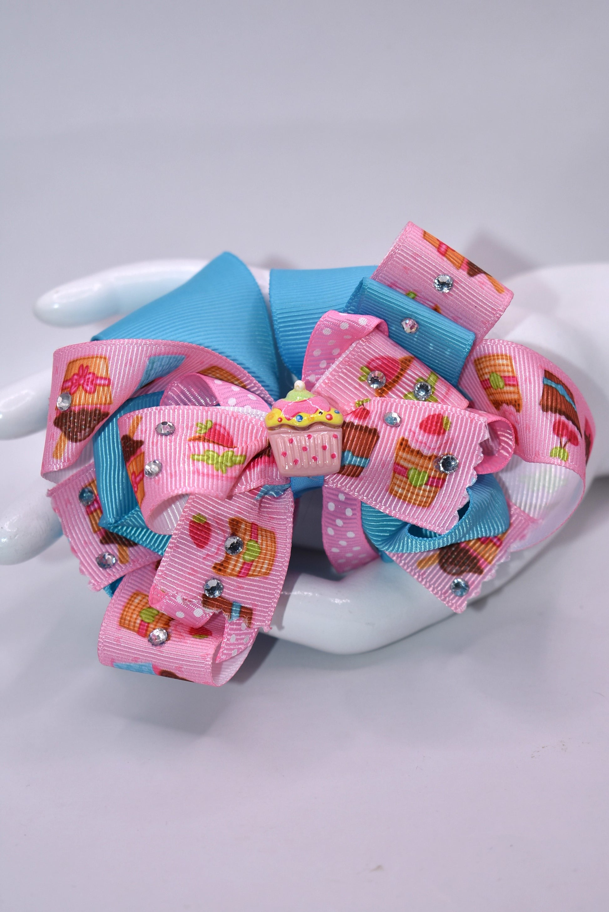 🧁 Sweet dreams come true with this adorable cupcake bow! Featuring layers of delightful cupcake-printed ribbon that stack for maximum cuteness, this accessory sparkles with dazzling crystals that catch the light beautifully. The precious little cupcake charm sits perfectly on top, adding that final touch of charm. Secured with a wrapped alligator clip, it's effortless to wear and removes easily whenever you want. Perfect for adding a sprinkle of sweetness to your day! 🎀✨