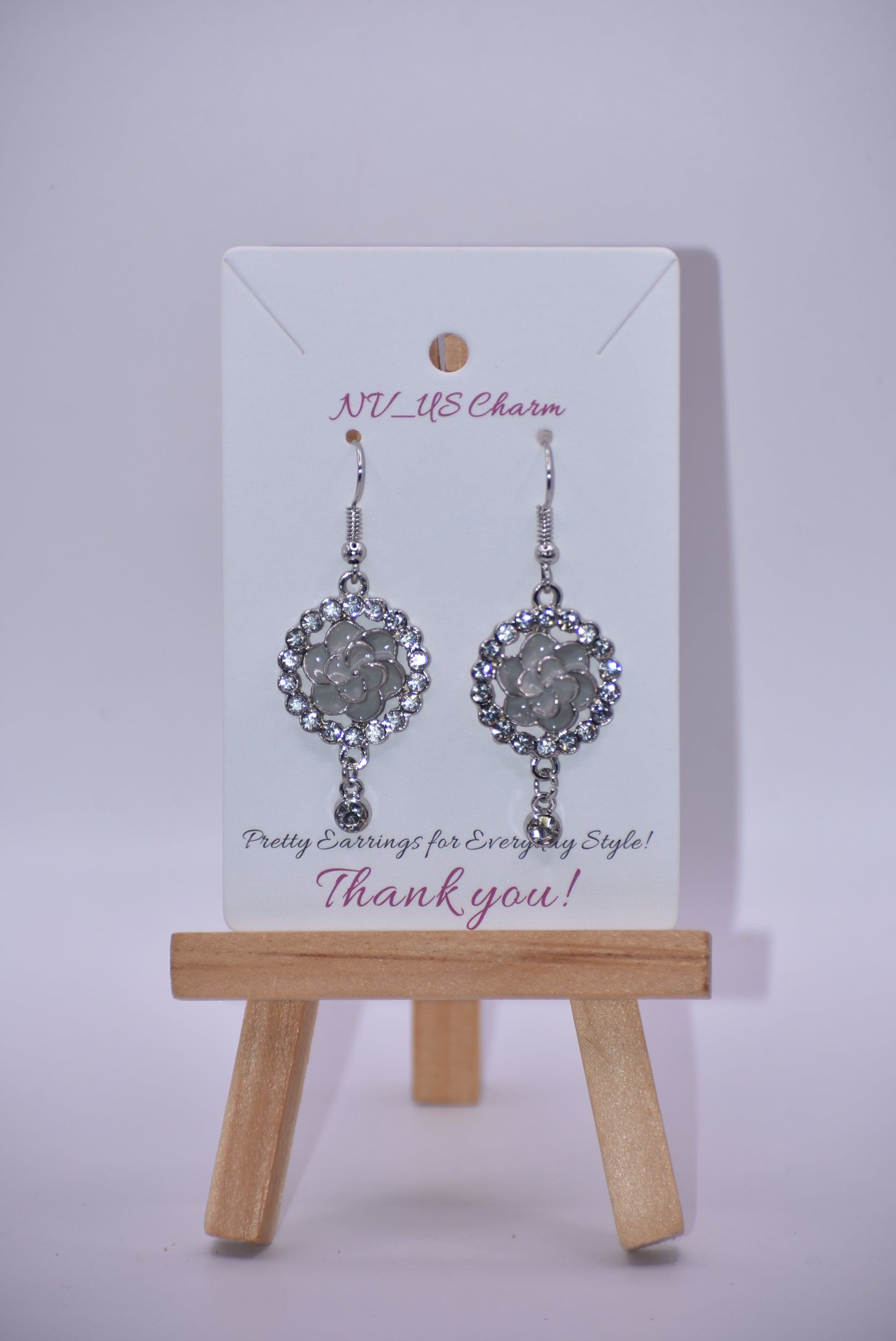 These Gray Collection 9 earrings provide a unique and sophisticated look. Featuring a pretty gray flower surrounded by crystals and a small crystal hanging, these silver hook earrings will add sparkle and elegance to any outfit. With intricate details and luxurious design, these earrings are a must-have addition to any jewelry collection.