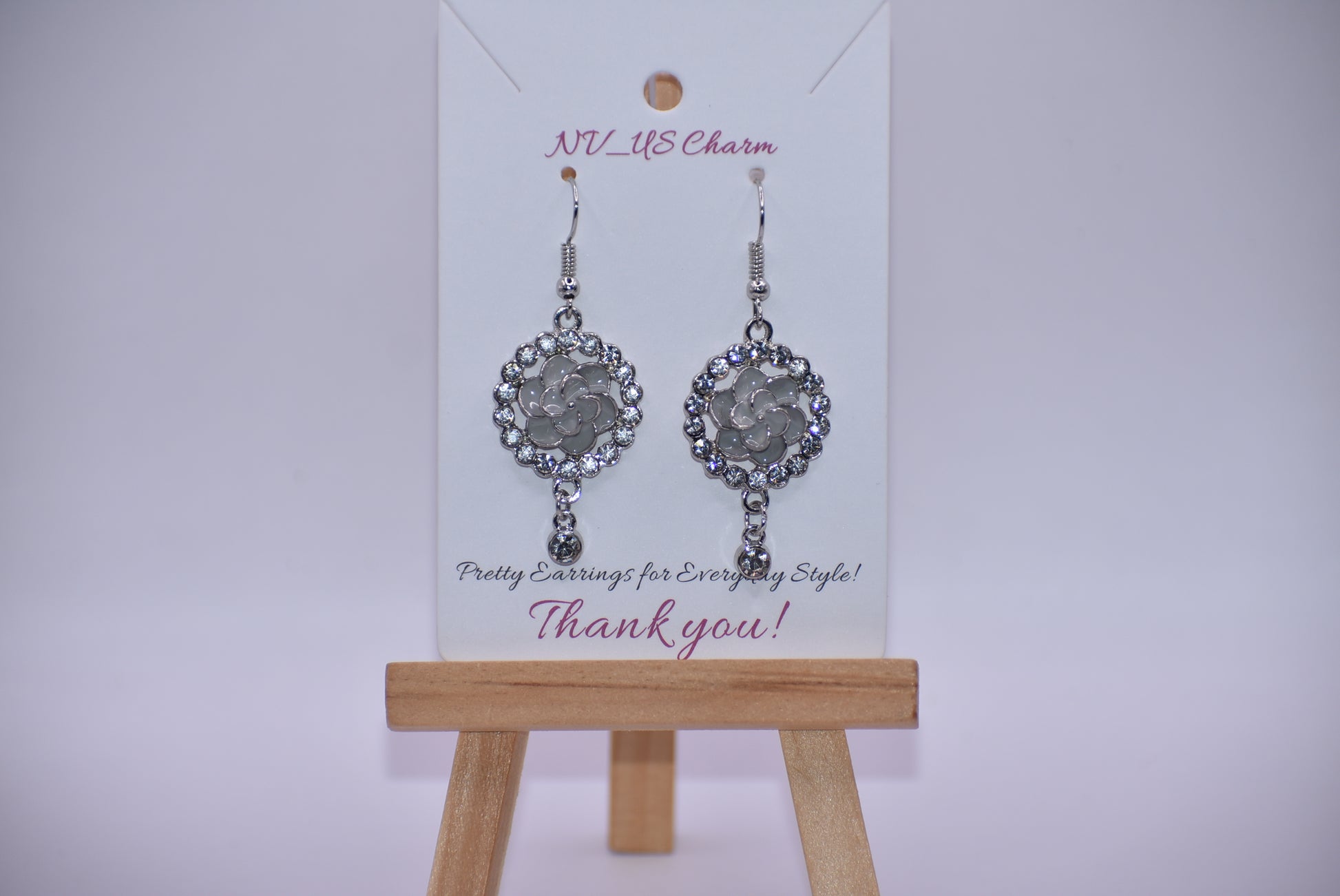 These Gray Collection 9 earrings provide a unique and sophisticated look. Featuring a pretty gray flower surrounded by crystals and a small crystal hanging, these silver hook earrings will add sparkle and elegance to any outfit. With intricate details and luxurious design, these earrings are a must-have addition to any jewelry collection.